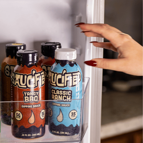 Hand reaching for a bottle of 'Saucified' Classic Ranch dipping sauce in a refrigerator.