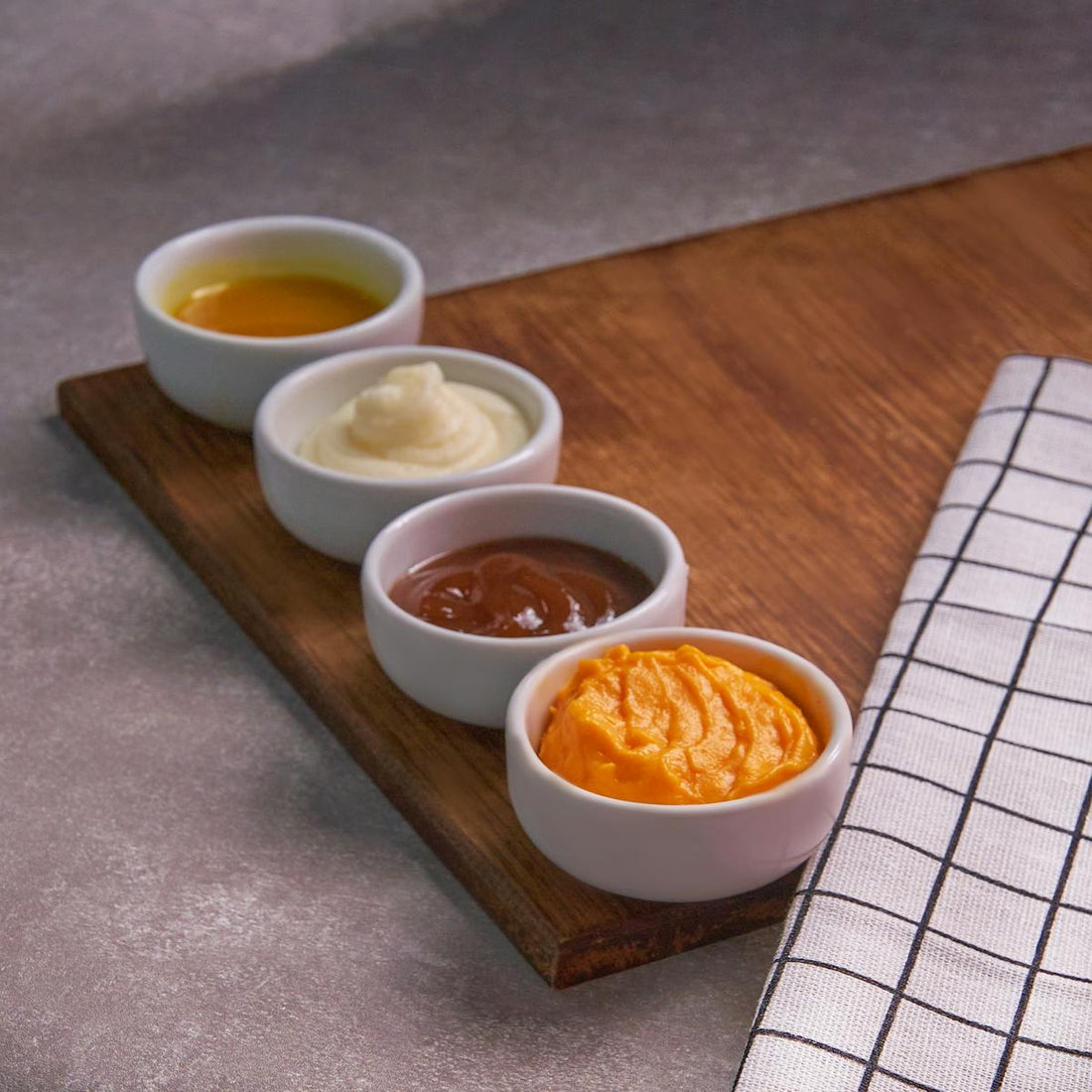 Four assorted low calorie dipping sauces displayed in ceramic bowls on a wooden board