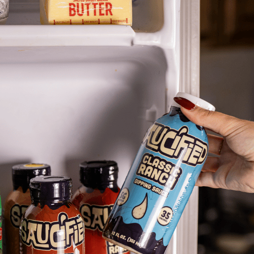 Hand holding a bottle of Classic Ranch dipping sauce in front of a refrigerator with various condiments.