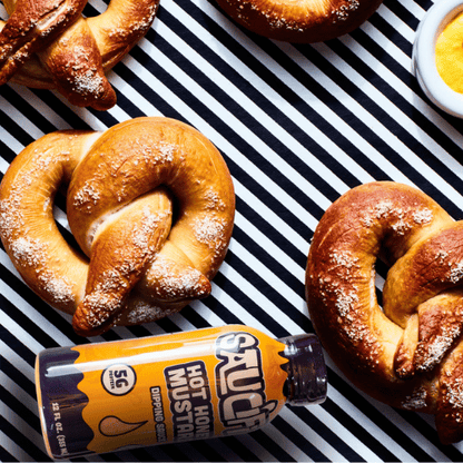  pretzels with a bottle of hot honey mustard on a black and white striped background