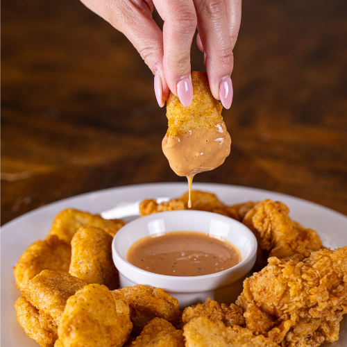 Chicken nugget being dipped into a small bowl of sauce on a plate.