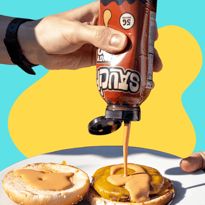 Hand pouring sauce from a bottle onto a cheeseburger on a colorful background